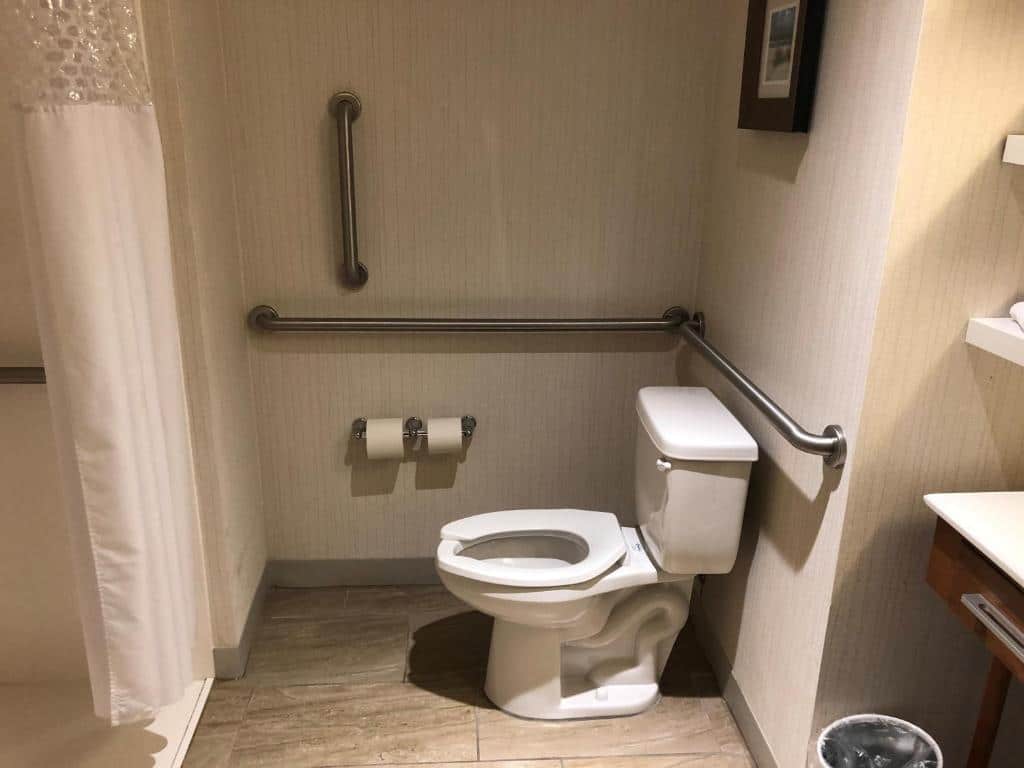 Banheiro adaptado do Hampton Inn & Suites by Hilton Tampa Busch Gardens Area com barras de apoio ao redor do vaso sanitário e um box de cortinas