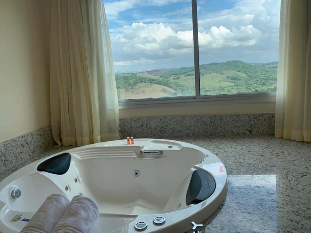 banheira de hidromassagem redonda do Hotel Mirante São Brás em São Brás do Suaçuí com uma janela grande ao lado e uma vista para o vale