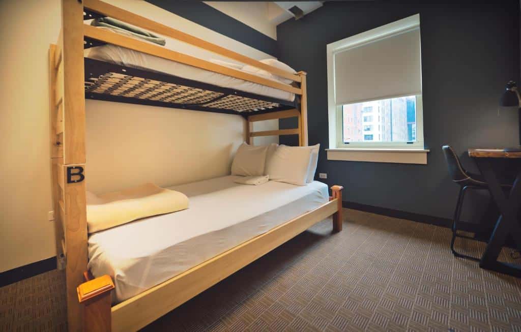 Quarto do HI Chicago Hostel com uma cama de beliche com cobertas brancas, no lado esquerdo, e no lado direito mesa de trabalho.