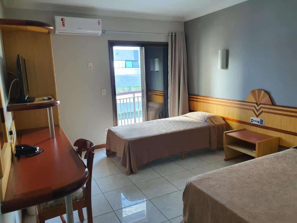 Quarto no Hotel Aquarius do Vale, em São José dos Campos, com duas camas de solteiro, cortina numa varandinha, além de móvel com uma pequena TV