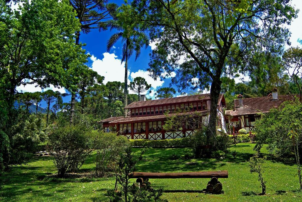 Casa grande e branca com detalhes de madeira e bastante árvores em volta durante o dia, ilustrando post pousadas em Visconde de Mauá.