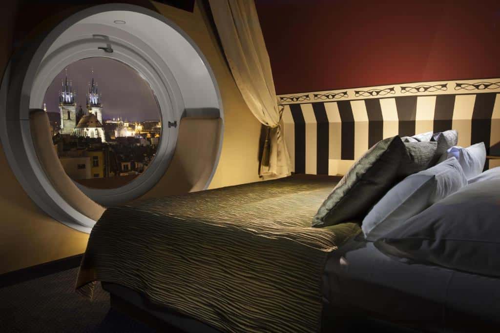 Quarto do Hotel Paris Prague com uma cama de casal de frente para uma ampla janela redonda com vista direta para pontos turísticos da cidade