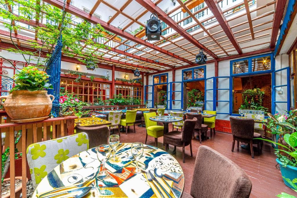 Área de refeições do Hotel Salvator com cadeiras coloridas, mesas redondas, muitas plantas ao redor, teto de vidro e janelas em tons de azul