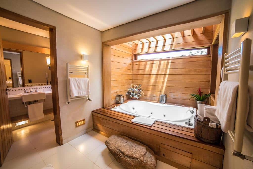 Banheiro amplo do Hotel Toriba  com uma banheira de hidromassagem com um pequeno deck ao redor com vasos de flores e toalhas brancas