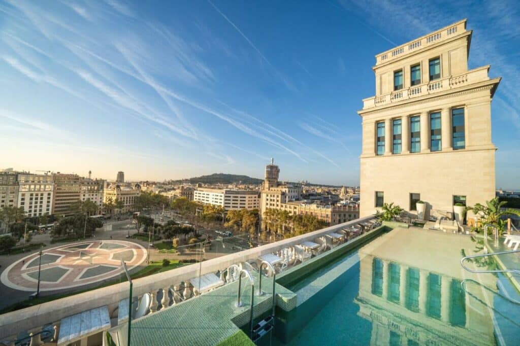 Piscina do Iberostar Selection Paseo de Gracia, um dos melhores hotéis em Barcelona. Há escadas para entrar na piscina, e um prédio bege na lateral direita.
Do lado esquerdo é possível vera Plaça de Catalunya e a cidade de Barcelona.