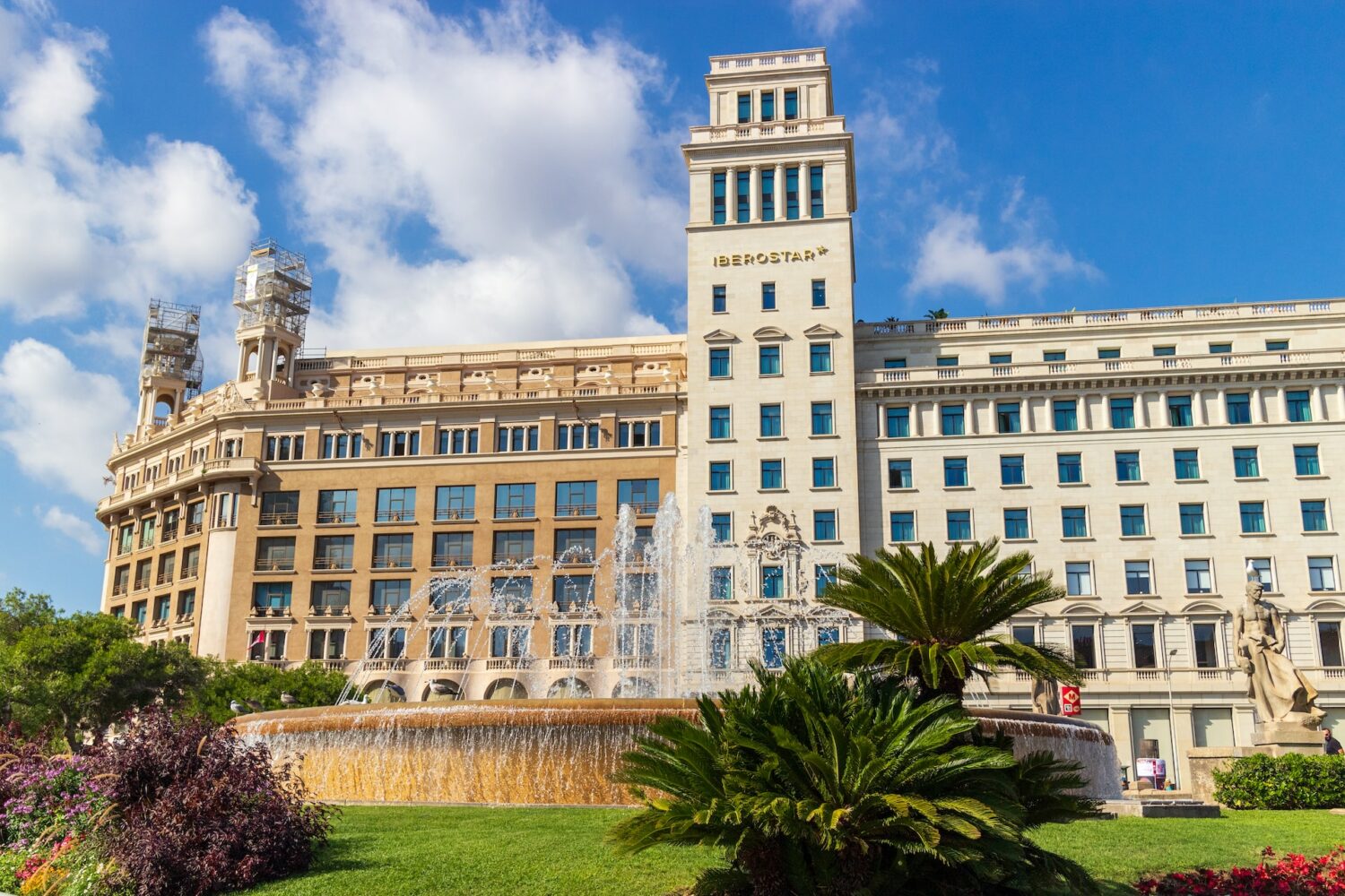 Fachada do hotel Iberostar, uma das recomendações de onde ficar em Barcelona. Há uma fonte na frente do hotel, e algumas plantas.