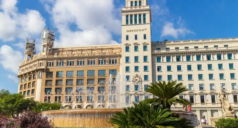 Fachada do hotel Iberostar, uma das recomendações de onde ficar em Barcelona. Há uma fonte na frente do hotel, e algumas plantas.