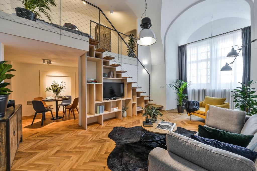 Sala de estar do Lazenska N°4 com uma escada que leva para o mezanino, há muitos sofás, um tapete, o chão é de madeira e a decoração é bem moderna