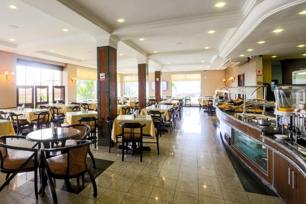 lounge do Hotel Exclusivo, um dos hotéis perto do Aeroporto de Curitiba, com mesas e cadeiras em tons marrons e bancada grande com café do manhã servido