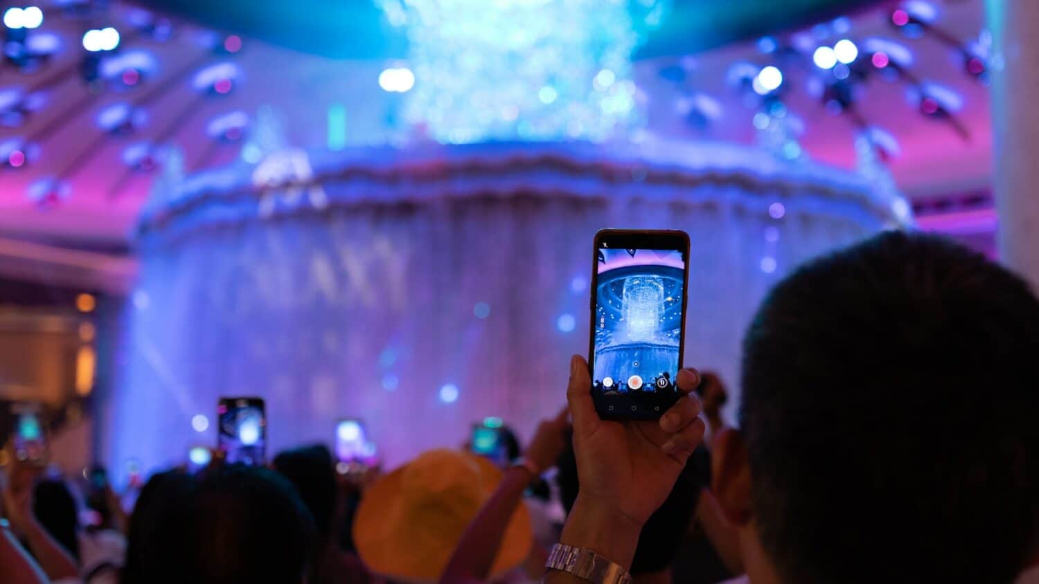 Pessoa segurando um celular para tirar uma foto de um show de fogos à frente, durante a noite.
