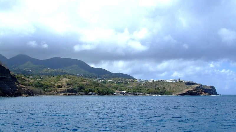 Ilha de Montserrat, com vegetação vasta e algumas construções na ilha cercada pela água azul do oceano em um dia azul com nuvens.