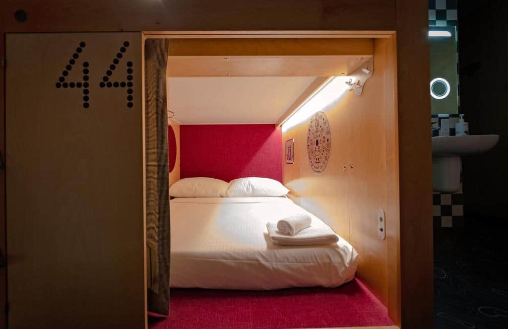 Quarto do Pangea Pod Hotel em formato de cápsula, com uma cama de casal dentro e umas toalhas em cima do local