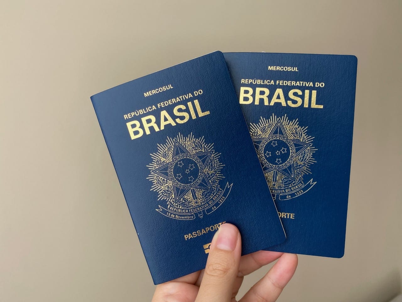 Capa azul marinho nos passaportes brasileiros, sendo uma mão segurando duas unidades do documento, para ilustrar a capa do post "como tirar passaporte"