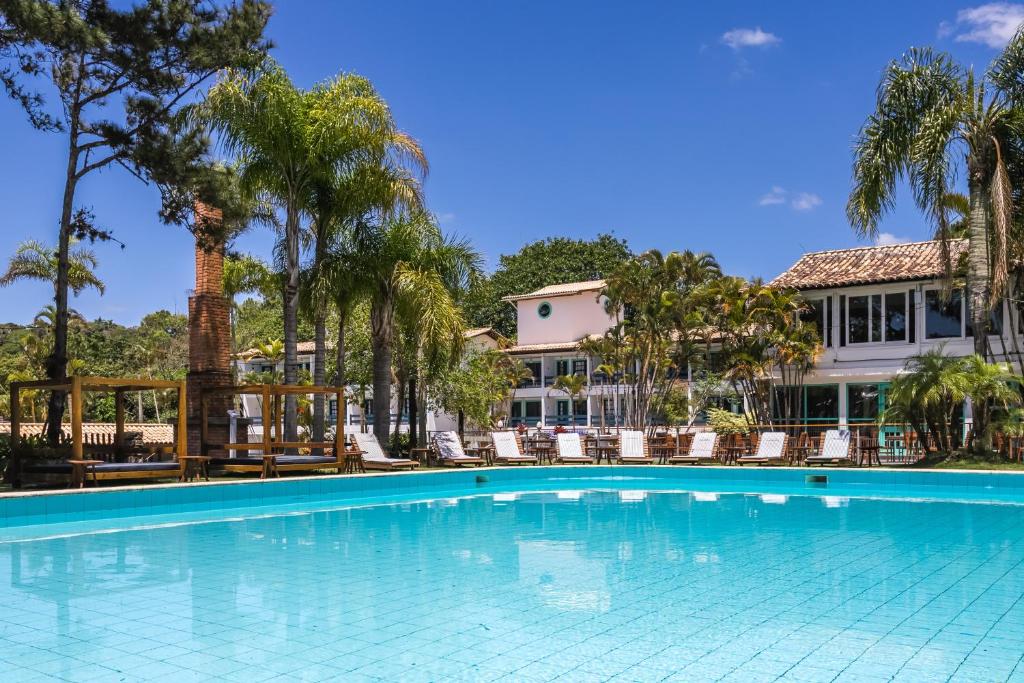 piscina do Selina Floripa, um dos hotéis perto do Aeroporto de Florianópolis, retangular, com espreguiçadeiras e palmeiras ao redor, com o hotel de paredes brancas ao fundo