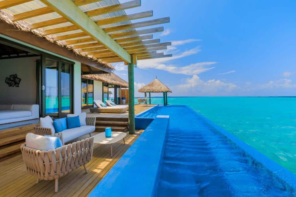 piscina que se liga ao mar no Velassaru Maldives, um dos resorts nas Maldivas, com varanda com sofá em branco e azul com detalhes em madeira bem chique