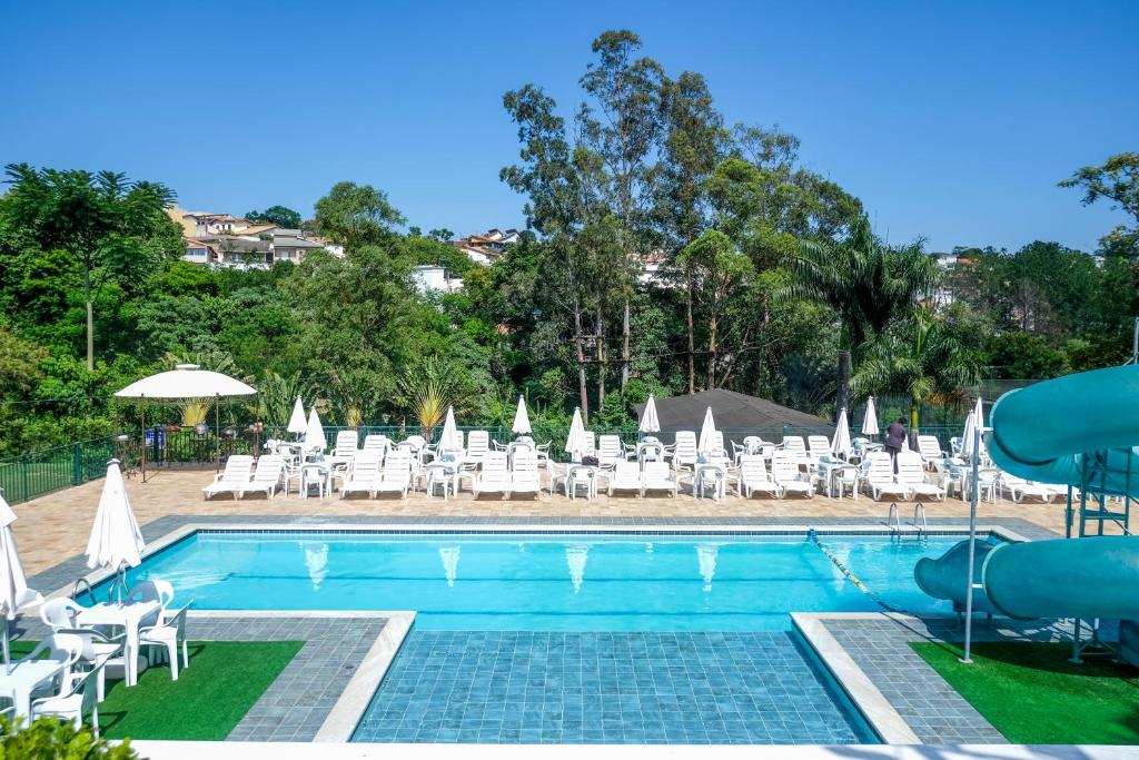 Piscina do Atibaia Residence Hotel & Resort durante o dia com cadeiras brancas do lado esquerdo e a piscina a frente. Representa hotéis em Atibaia.