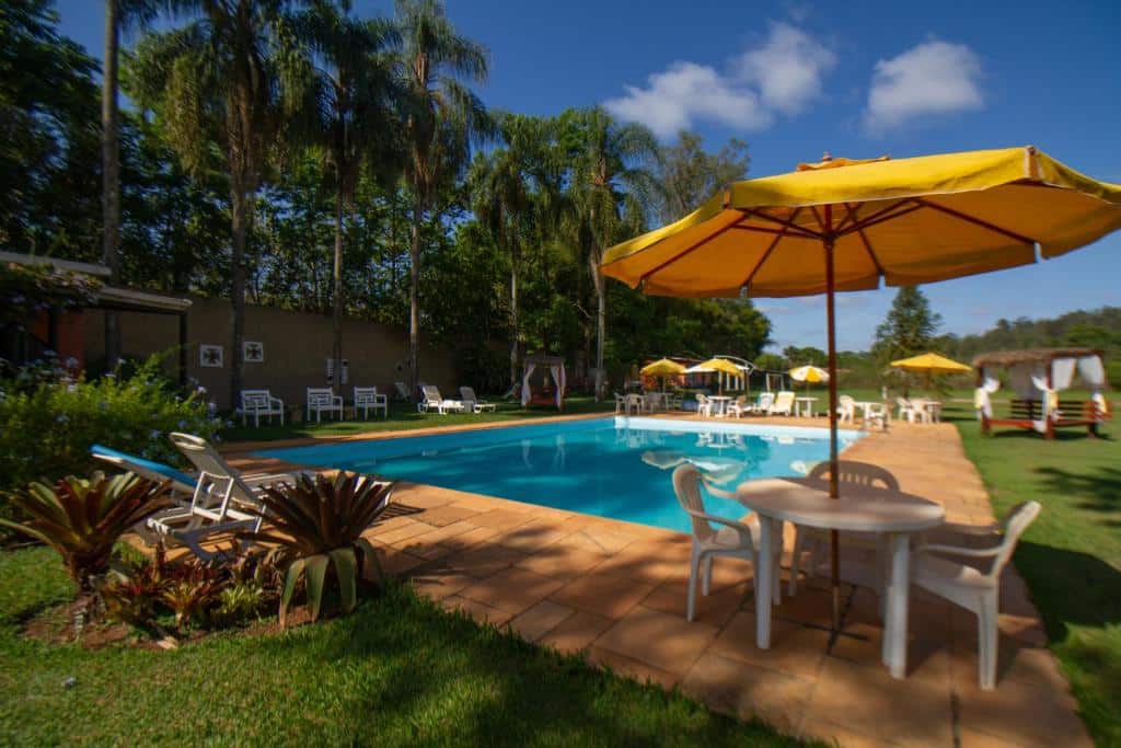 Piscina da Estância Canaã durante o dia com cadeiras brancas em volta da piscina. Representa resorts em Atibaia.