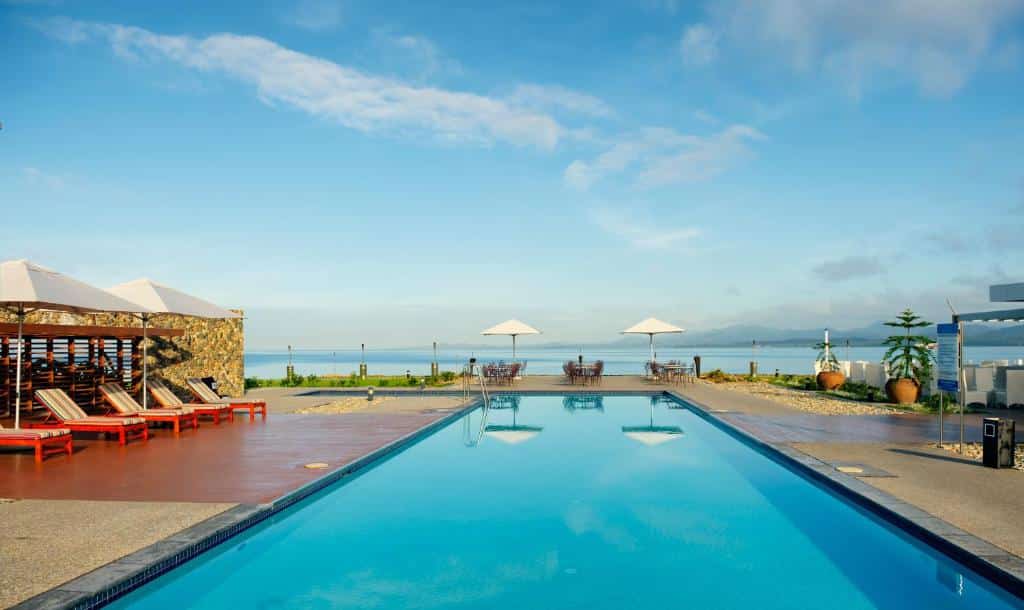 Vista da piscina do Grand Pacific Hotel durante o dia com cadeiras do lado esquerdo perto da piscina e a piscina tem vista do mar. Representa hotéis em Fiji.