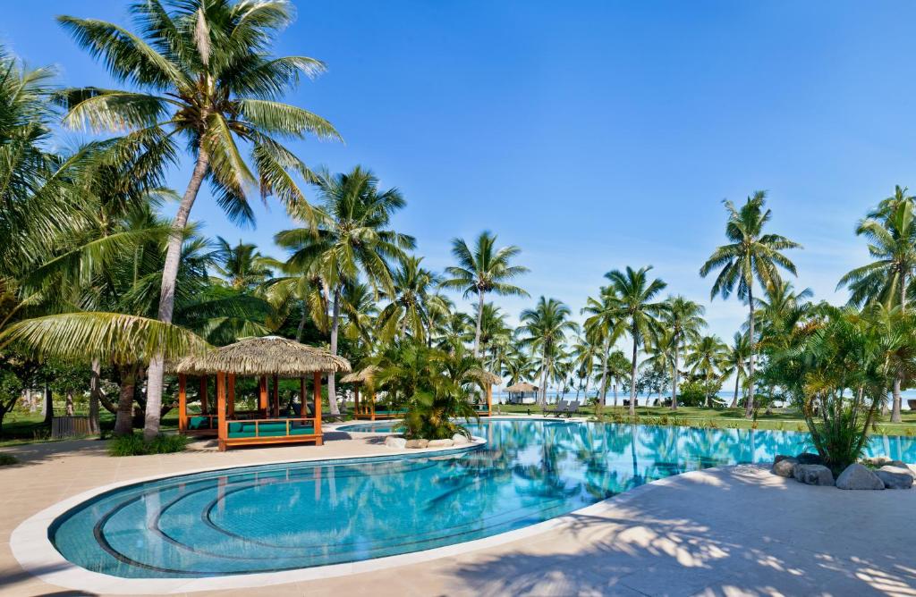 Vista da piscina do Lomani Island Resort – Adults Only durante o dia com vários coqueiros em volta. Representa hotéis em Fiji.