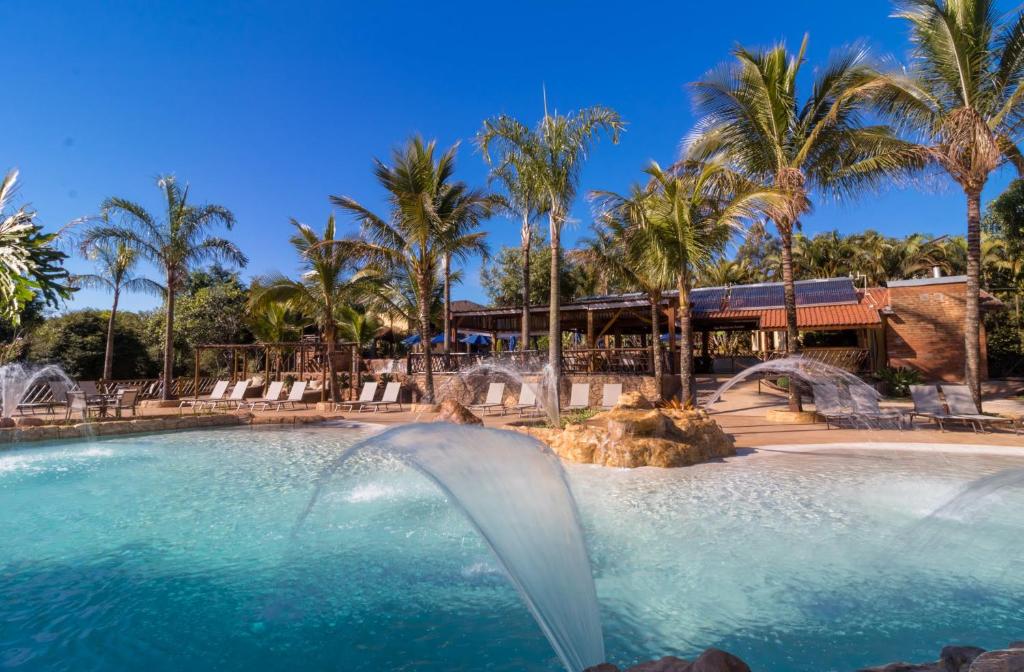 Vista da piscina do Recanto Alvorada Eco Resort durante o dia, com cadeiras no lado esquerdo e, logo ao fundo, a hospedagem. Representa chalés em Brotas.