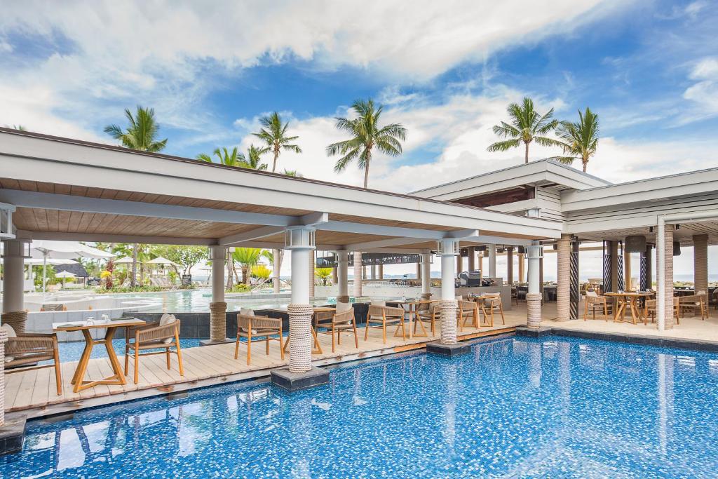 Vista da piscina do Sheraton Fiji Golf & Beach Resort durante o dia com cadeiras e mesa em volta. Representa hotéis em Fiji.