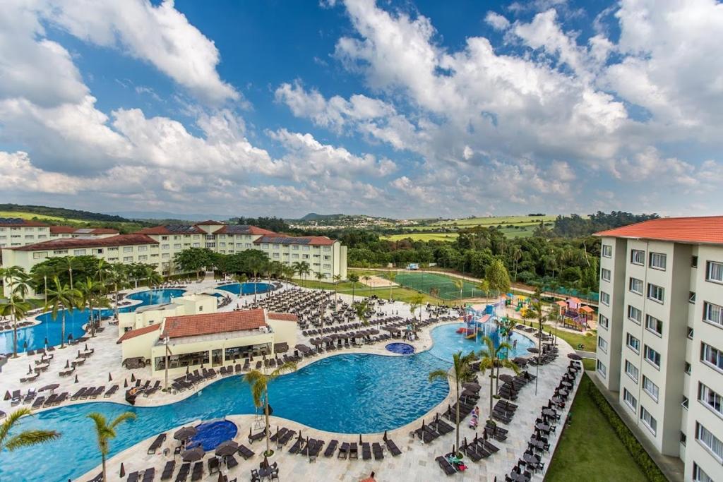 Vista de cima da piscina do Tauá Hotel & Convention durante o dia com cadeiras em volta, coqueiros e a hospedagem. Representa resorts em Atibaia.