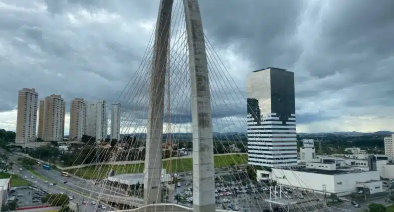 Uma moderna ponte estaiada com um arco alto atravessa uma área urbana movimentada com prédios altos sob um céu nublado, para representar hotéis em São José dos Campos.