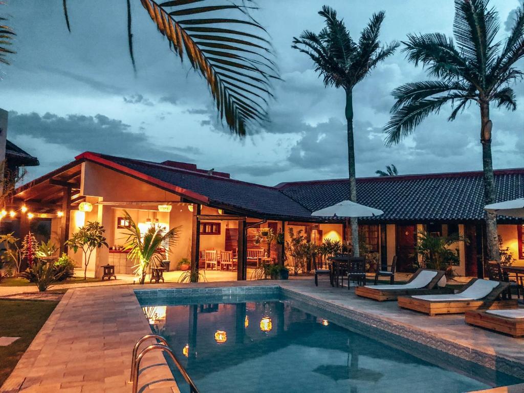 área externa da Casa Mar Campeche, em Floripa, com piscina retangular grande ao entardecer, com várias luzes na estrutura da pousada em madeira com algumas palmeiras ao redor