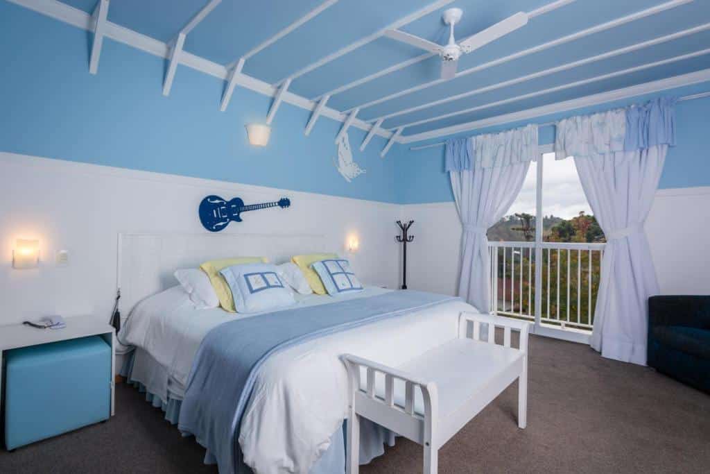 Quarto da Pousada Piano Piano pintado em azul bebê e branco, uma cama de casal, uma sacada ampla, há uma mesinha de cabeceira branca e um bufê azul