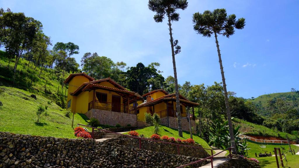 Casas amarelas no morro de gramado verde com árvores em volta durante o dia, ilustrando post pousadas em Visconde de Mauá.