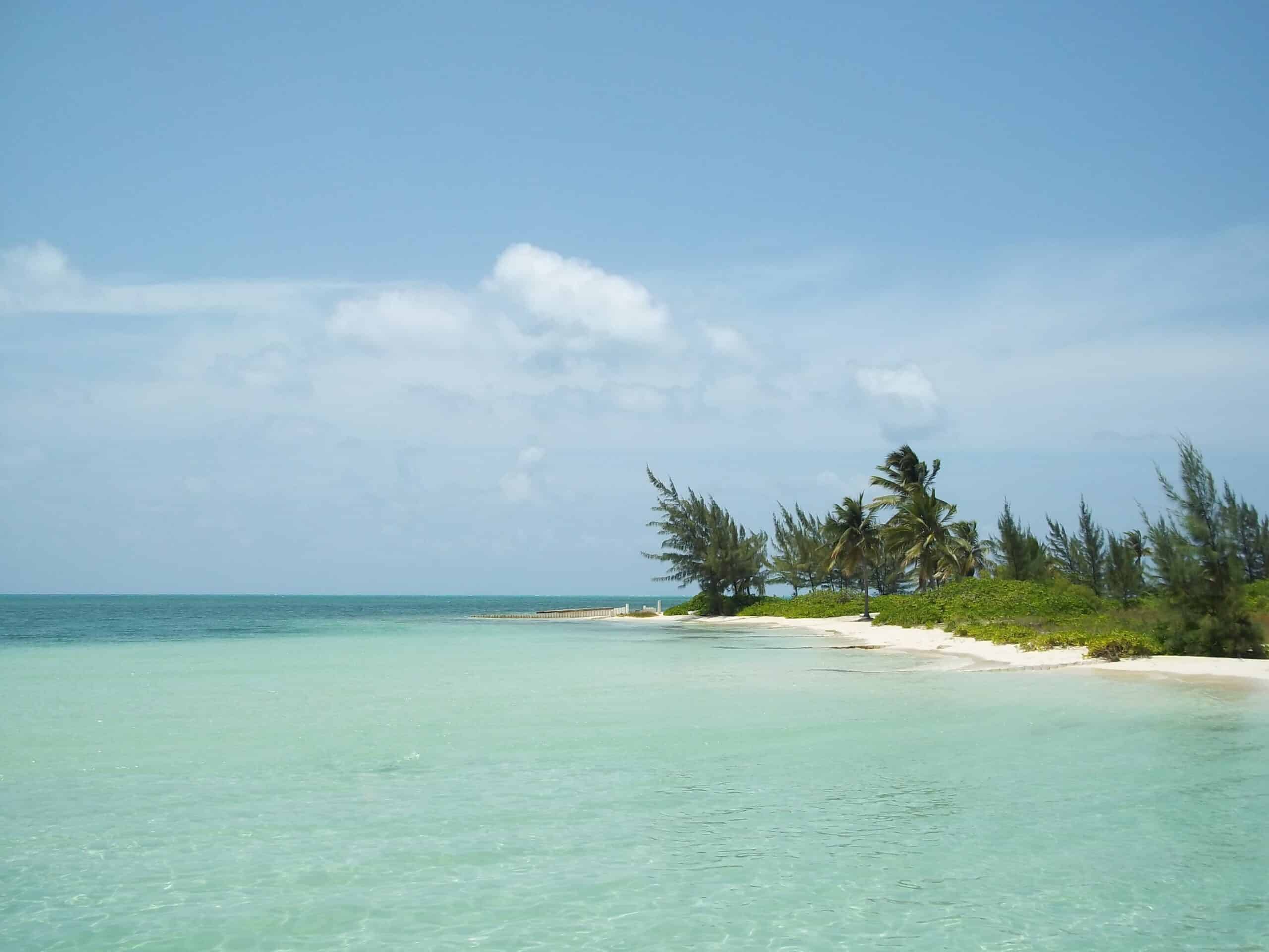 Vista da praia das Ilhas durante o dia com mar azul claro, do lado direito uma pequena parte da ilha com areias brancas e árvores.