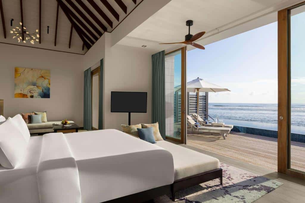 quarto do Radisson Blu Resort Maldives com cama de casal grande e decoração chique minimalista, há uma tv e varanda grande com espreguiçadeiras e piscina que liga até o mar