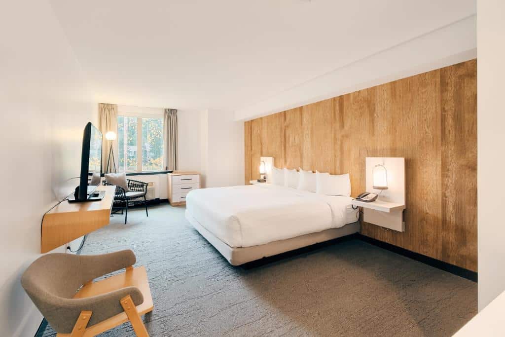 Quarto do Aava Whistler Hotel com uma cama de casal, uma janela com cortinas, uma televisão e uma poltrona, o chão é de carpete e duas mesinhas de cabeceira com abajur