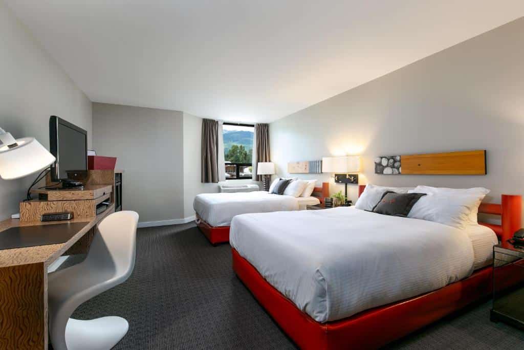 Quarto do  Adara Hotel com duas camas, uma de solteiro e uma de casal, uma bancada com cadeira, além de uma televisão e uma janela com cortinas, hotéis perto do Whistler