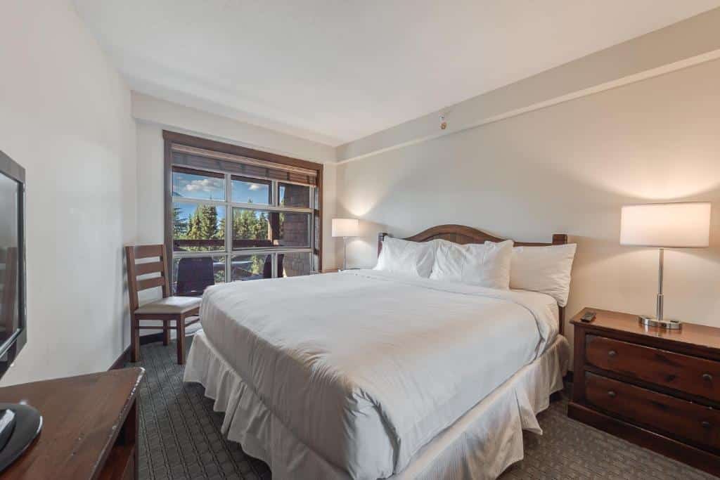 Quarto do Blackcomb Springs Suites by CLIQUE com uma varanda com vista para as montanhas, uma cama de casal, uma mesinha de cabeceira com abajur