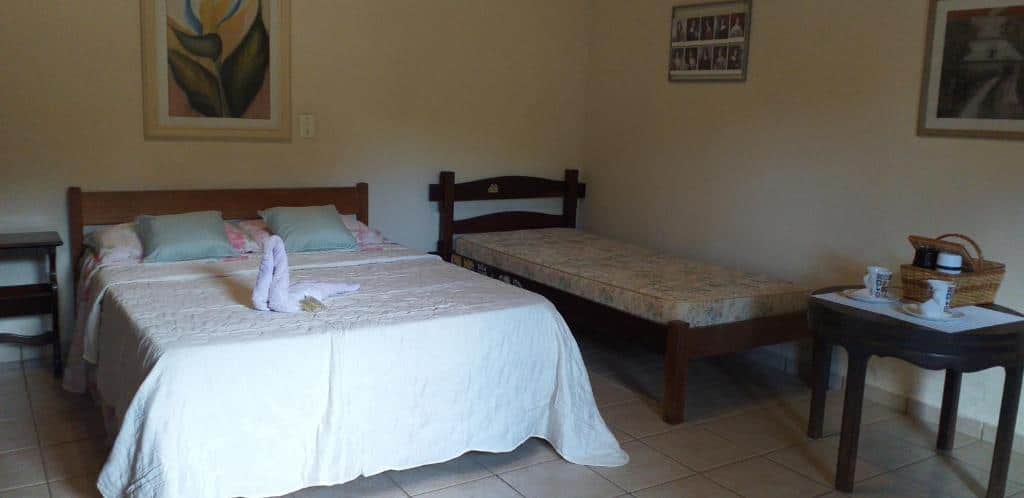 Quarto do Chalé e Camping Daragona 1, com cama de casal do lado esquerdo e uma cama de solteiro do lado direito e uma mesa redonda de madeira em frente a cama de solteiro.