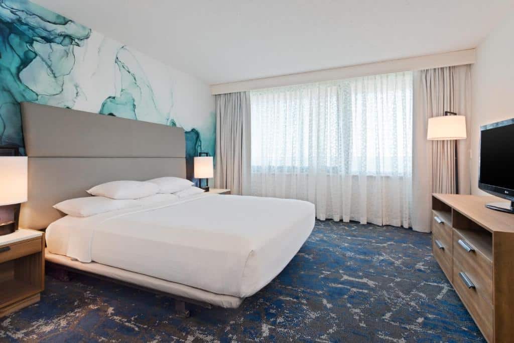 Quarto no  Embassy Suites by Hilton Tampa USF Near Busch Gardens com uma cama de casal, um carpete, uma janela com cortinas, um móvel com gavetas com uma televisão em cima
