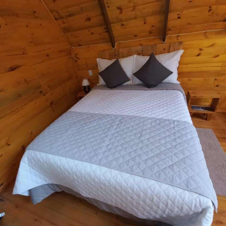 cama de casal com dois travesseiros brancos e duas almofadas cinza dentro do chalé