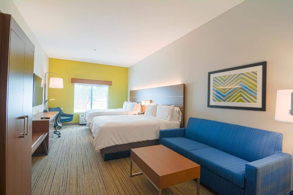 Quarto do Holiday Inn Express Hotel & Suites Tampa-USF-Busch Gardens, an IHG Hotel com uma cama de casal e uma de solteiro, uma janela com persianas, um sofá azul e uma mesinha de centro, uma poltrona, televisão e um pequeno armário com duas portas