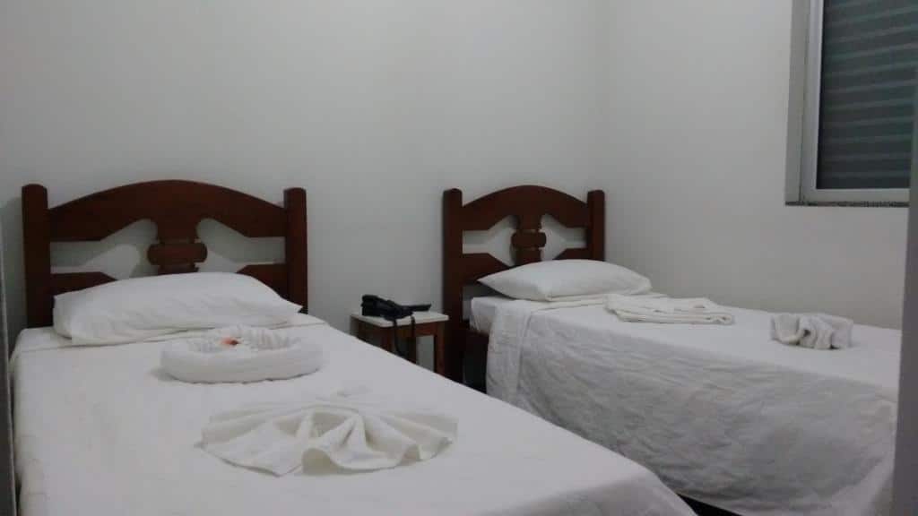 quarto do Hotel Brasil Real com duas camas de solteiro e uma cômoda com telefone entre as duas. Há toalhas e lençóis brancos em cada uma