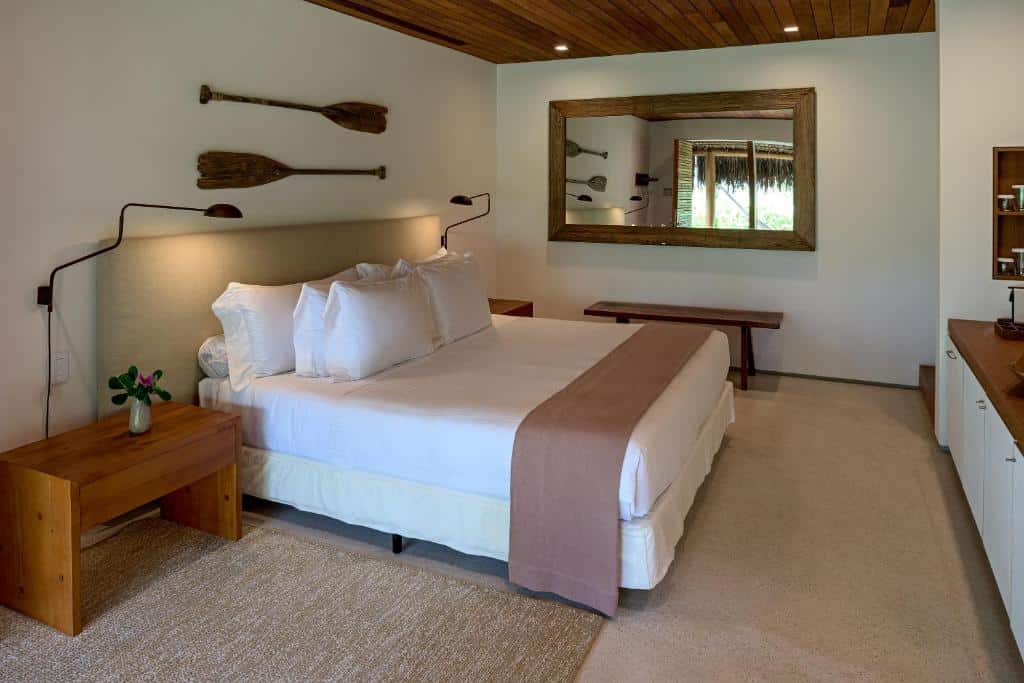 Quarto do Hotel Fasano Trancoso com cama de casal, duas cômodas de madeira com luminária e uma cômoda de madeira em frente a cama.