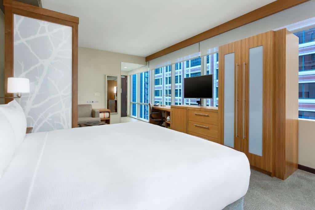 Quarto do Hyatt Place com cama, em frente a cama um guarda roupa, uma cômoda de madeira com TV em cima.