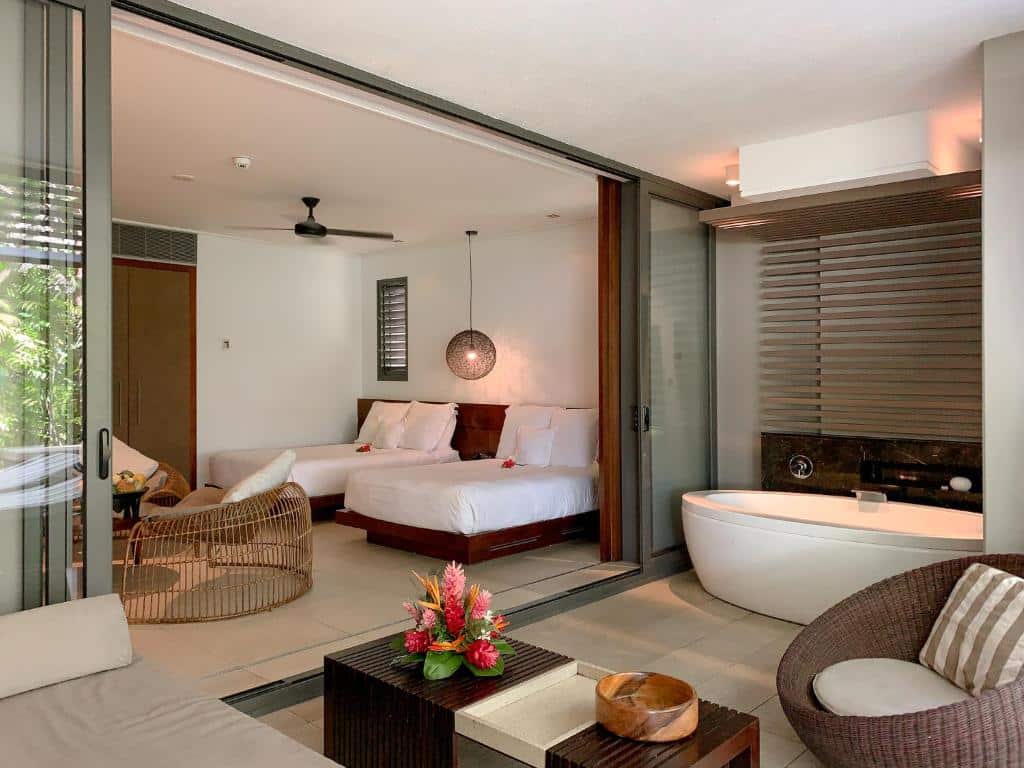 Quarto do InterContinental Fiji Golf Resort & Spa com banheira redonda do lado direito com poltrona e mesa de centro do lado esquerdo duas camas de solteiro com duas poltronas em frente as camas.