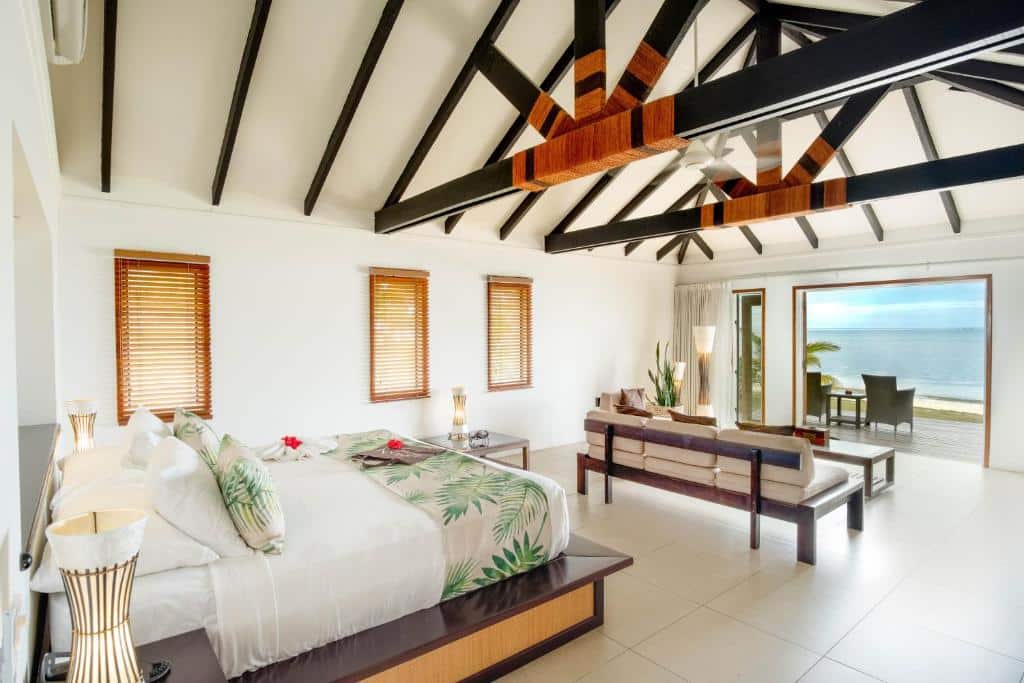 Quarto do Lomani Island Resort – Adults Only  com cama de casal ao centro com duas cômodas ao lado com luminária, em frente uma área de estar com sofá e vista para o mar.