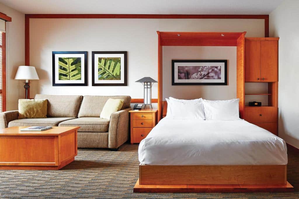 Quarto do Pan Pacific Whistler Mountainside com uma cama de casal, um sofá com dois lugares, uma mesinha de cabeceira com abajur e uma mesinha de centro