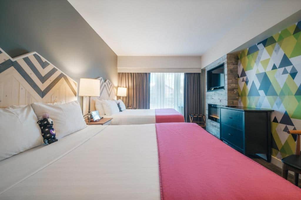 Quarto do Summit Lodge Boutique Hotel Whistler com uma cama de casal, uma de solteiro, uma janela com cortinas, um lareira, uma televisão e uma cômoda com duas gavetas