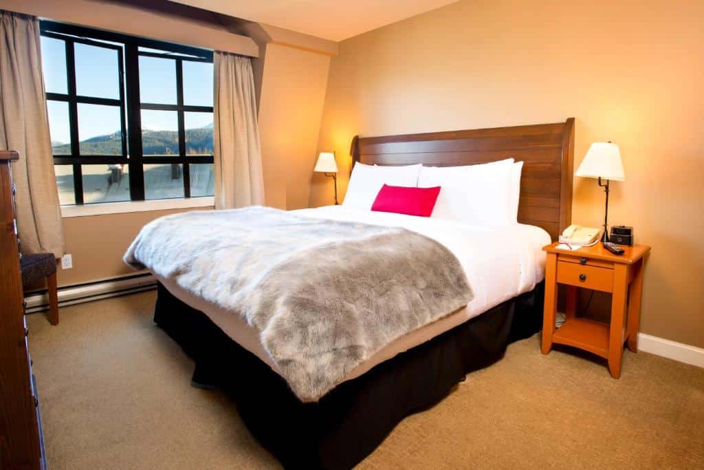 Quarto do Sundial Hotel com cama de casal, janelas com cortinas, carpete no chão e uma mesinha de cabeceira com abajur, para representar hotéis em Whistler