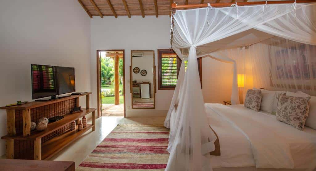 Quarto do Hotel e Resort Villas de Trancoso com cama do lado direito com mosqueteiro em frente a cama cômoda com TV.