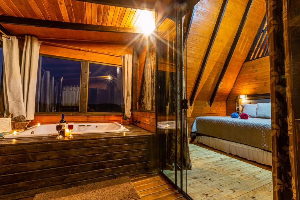 interior do Vale Chalés com uma banheira de hidromassagem à esquerda e uma cama de casal à direita. A decoração é rústica com muitos elementos em madeira crua.