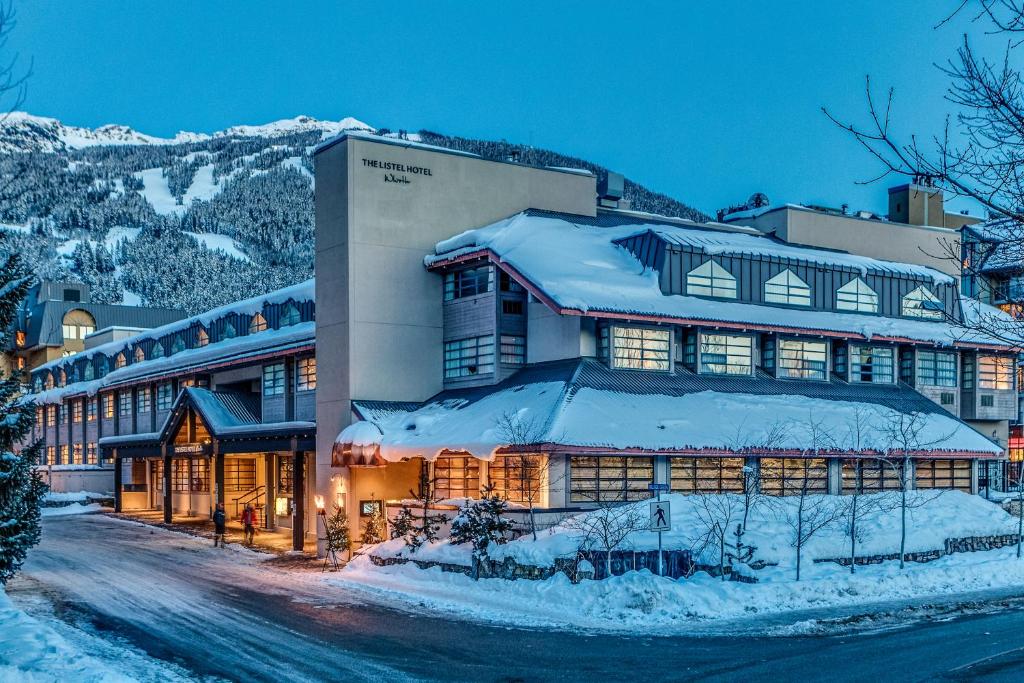Propriedade do The Listel Hotel Whistler com três andares, montanhas ao fundo com neve, assim como as ruas e a entrada do local